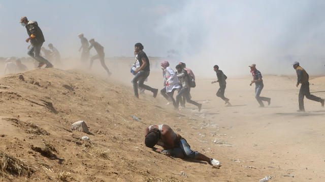 Palestinian demonstrator reacts as others run from tear gas fired by Israeli forces during a protest marking the 70th anniversary of Nakba, at the Israel-Gaza border in the southern Gaza Strip 