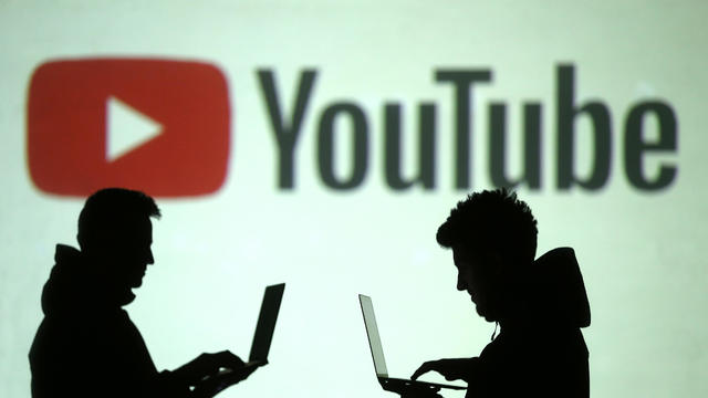 Silhouettes of mobile device users are seen next to a screen projection of Youtube logo in this picture illustration 