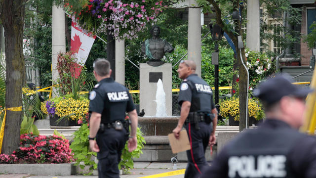 Police officers walk past Alexander the Great Parkette after a mass shooting in Toronto 