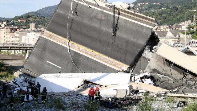 Firefighters and rescue workers stand next to collapsed motorway part at Morandi Bridge site in Genoa 