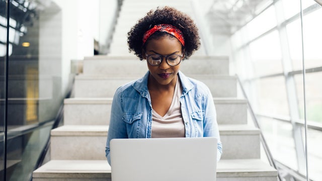 Focused young African student sitting on stairs using a laptop 