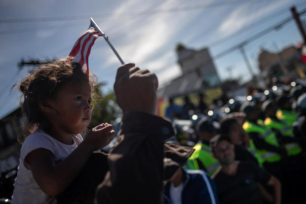 A migrant girl, part of a caravan of thousands from Central America, sits on top of her father as they are surrounded by police while marching to the United States border with Mexico in Tijuana 