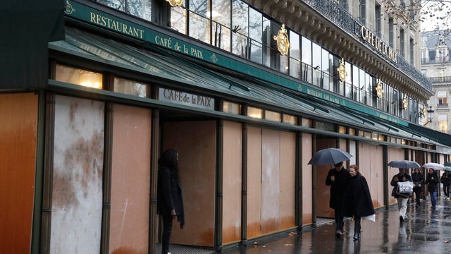 Pedestrians walk past wood panels protecting the "Cafe de la Paix" on the eve of a "yellow vests" protest in Paris 