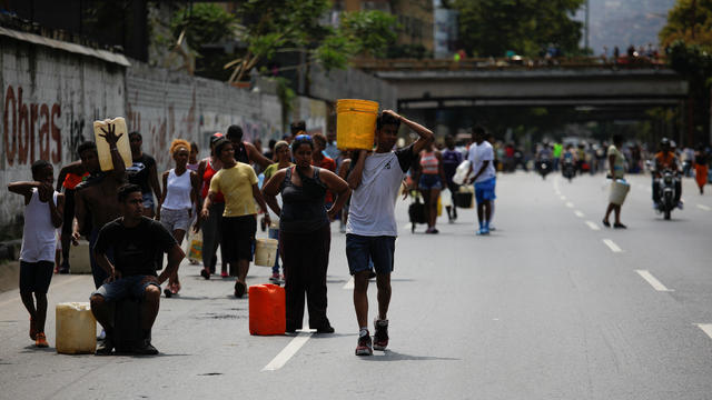 People walk on a highway, carrying containers with water collected from a sewage drain in Caracas 