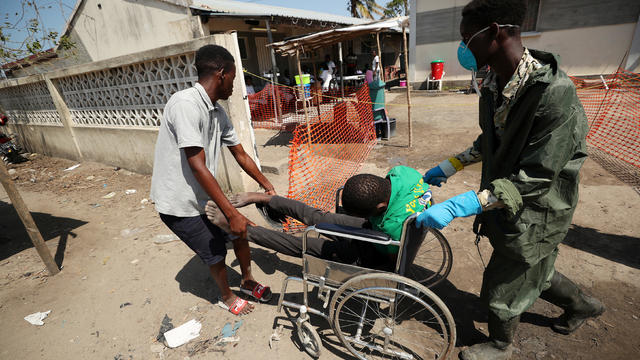 A medical staff member wears a protective mask as he assists a man arriving at a cholera treatment centre set up in the aftermath of Cyclone Idai in Beira 