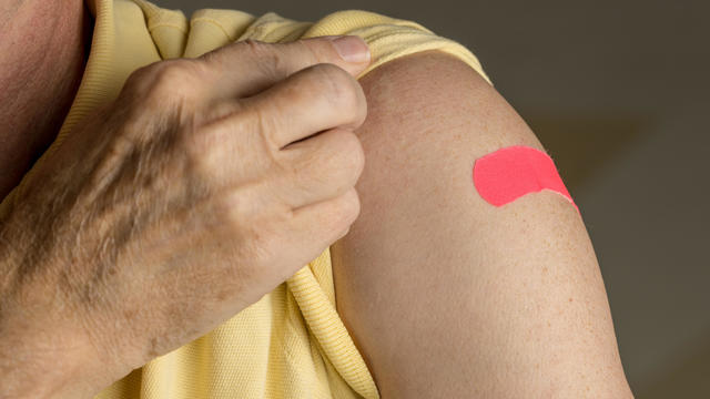 Senior man holding up shirt after flu injection 