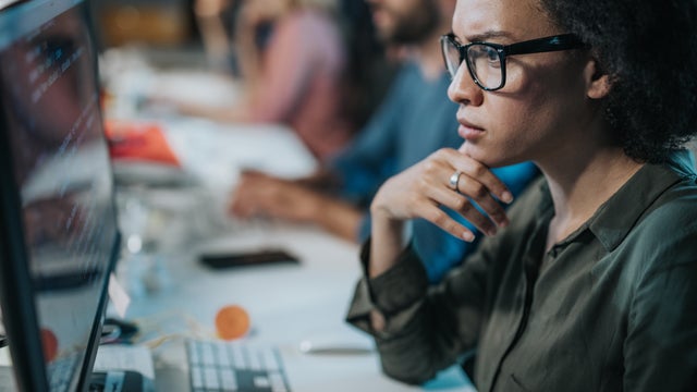 Concentrated African American woman brainstorming while coding data on desktop PC. 