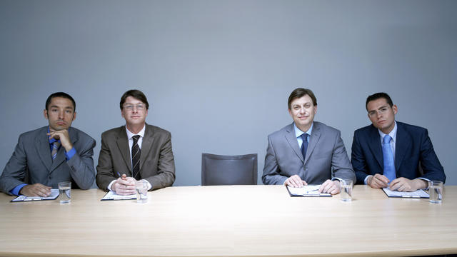 Four businessmen sitting next to empty chair in boardroom, portrait 