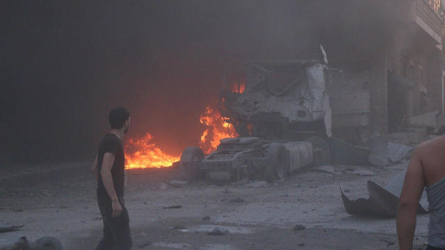 People walk next to fire, debris and a damaged truck after a deadly airstrike, said to be in Maarat al-Numan 