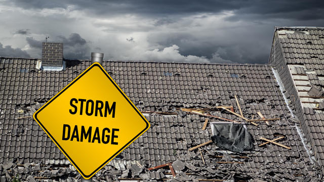 yellow damage warning sign in front of storm damaged roof of house 