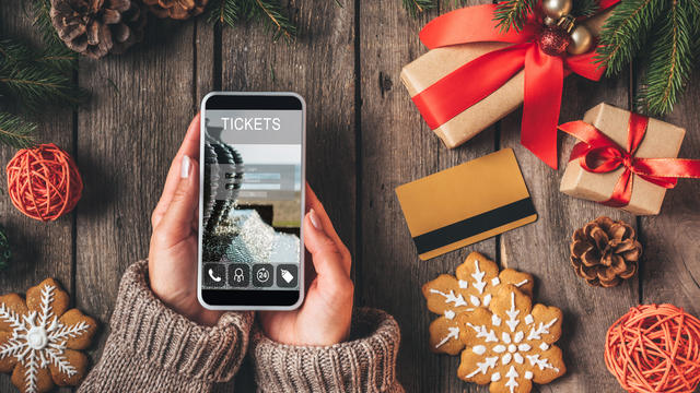 cropped view of woman using smartphone with ticket app on wooden background with credit card and christmas presents 