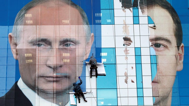 FILE PHOTO: Workers attach a pre-election poster featuring Russia's President Dmitry Medvedev (R) and Prime Minister Vladimir Putin, appealing to people to vote for the United Russia political party, onto an office building in the southern city of Krasnod 