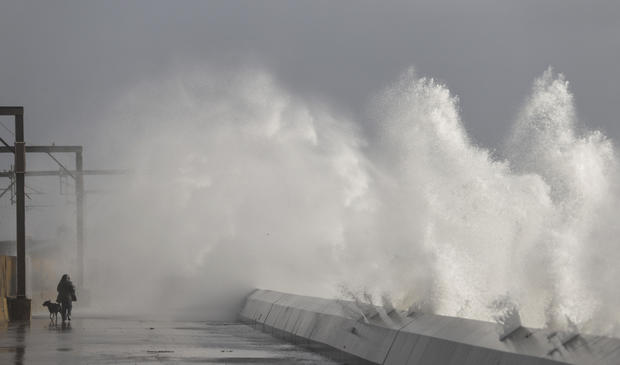A man takes his dog for a walk as waves hit the sea wall in Saltcoats, Scotland 