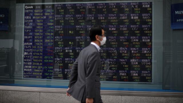 A man wearing protective face mask walks in front of a stock quotation board outside a brokerage in Tokyo 