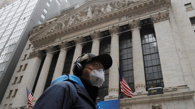 A man in a surgical mask walks by the New York Stock Exchange (NYSE) after more cases of coronavirus were confirmed in New York City, New York 