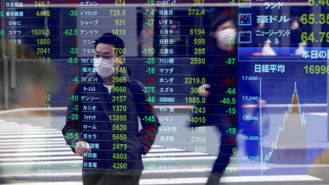 Passersby wearing protective face masks are reflected on a screen displaying stock prices outside a brokerage in Tokyo 