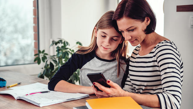 Mother using smart phone and helping daughter with homework 