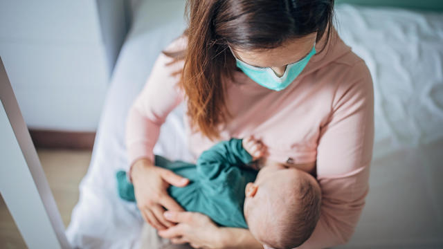 Mother with protective mask breastfeeding baby 