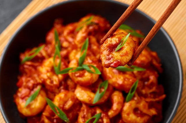 Schezwan Prawns in black bowl at dark slate background. Schezwan Prawns is indo-chinese cuisine curry dish with prawns or shrimps roasted in Schezwan Sauce. 