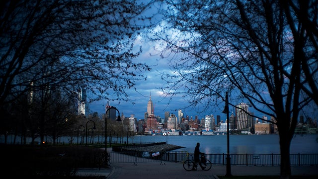A man pushes his bike in a closed park as the New York City skyline of Manhattan and the Empire State Building are seen during the outbreak of the coronavirus disease (COVID-19) in New York City, as seen from Weehawken 