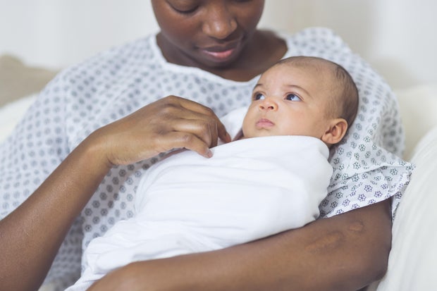 Beautiful African American mother in a hospital gown holds her newborn baby gently to her chest