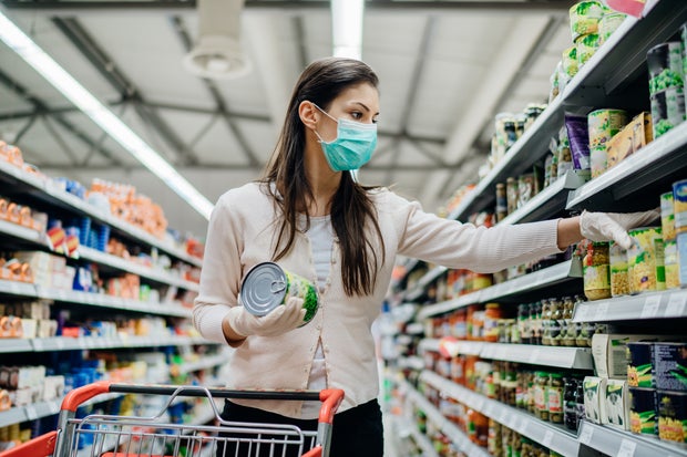 face mask Woman preparing for pathogen virus pandemic spread quarantine.Choosing nonperishable food essentials.Budget buying at a supply store.Pandemic quarantine preparation.Emergency to buy list