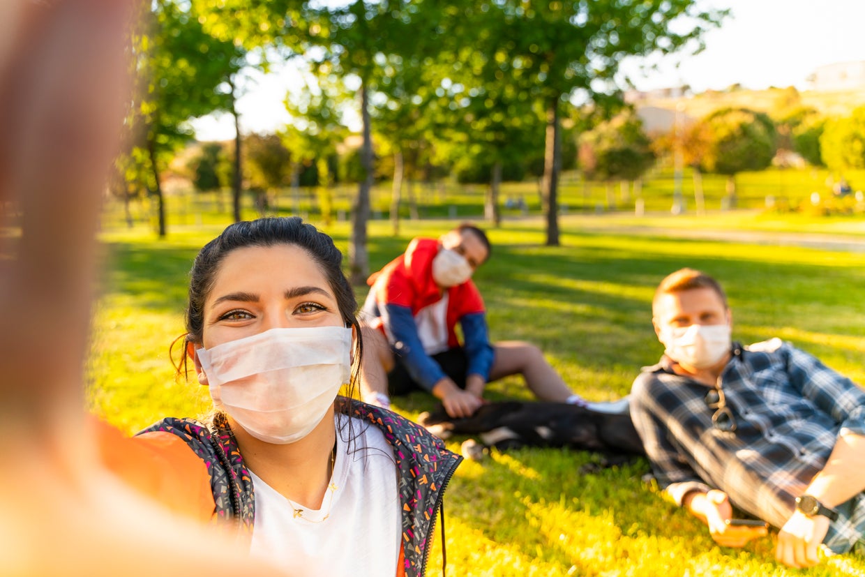face mask Cheerful university student taking selfie with friends sitting on grass 