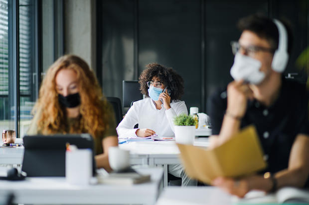 Young people with face masks back at work or school in office after lockdown. 