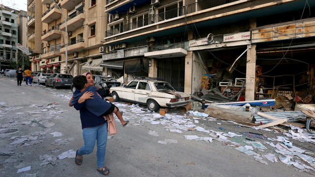 A woman carries a child as she walks past damaged shops following Tuesday's blast in Beirut 