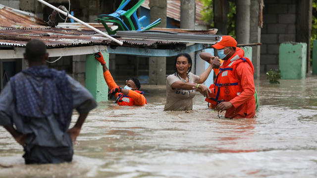 Members of the Civil Defence help a woman in a flooded street after the passage of Storm Laura, in Azua 