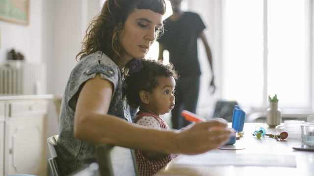 Woman working while sitting with daughter at table in house 