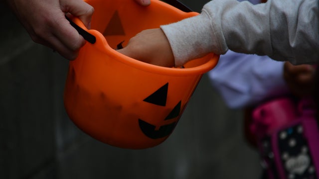 Cropped Image Of Hands Picking Candy From Halloween Basket 
