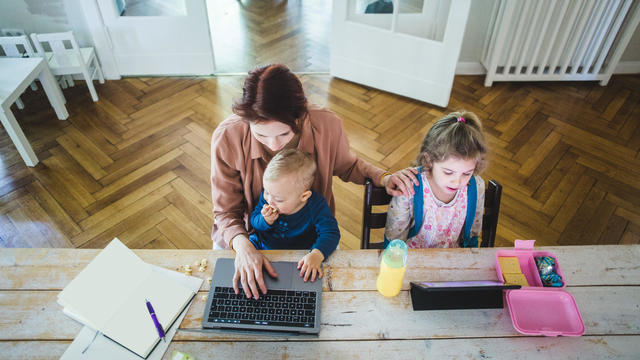 High angle view of mother working on laptop while sitting with cute son by daughter using digital tablet at table 