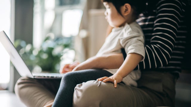 Cropped shot of a young Asian mother using laptop and working from home while taking care of little daughter in self isolation during the Covid-19 health crisis 