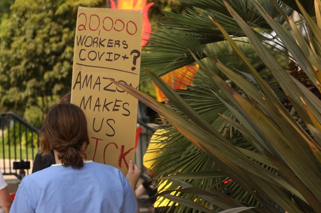 Protester holds a sign reading, "20,000 workers COVID+? Amazon makes us sick." 
