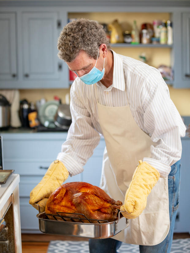 Mature Adult Man Cooking Thanksgiving Turkey Dinner Wearing COVID-19  PPE Face Mask 