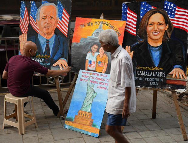 A man walks past an artist painting portraits of Joe Biden and Kamala Harris 