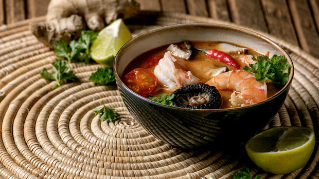 Traditional spicy Thai soup tom yum kung with shiitake mushrooms and prawns. ingredients above on straw wicker napkin over wooden plank table. 
