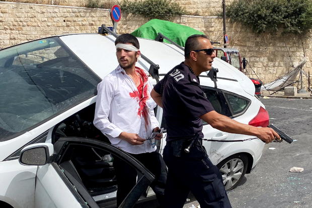 An Israeli police officer holds his weapon as he stands in front of an injured Israeli driver moments after witnesses said his car crashed into a Palestinian on a pavement during stone-throwing clashes near Lion's Gate just outside Jerusalem's Old City 