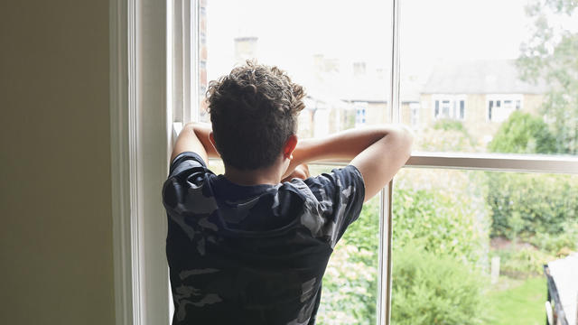 Teenage boy looking out of bedroom window 