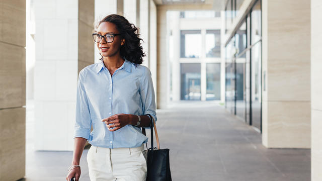 Female business professional walking outside an office building with bag on a hand 