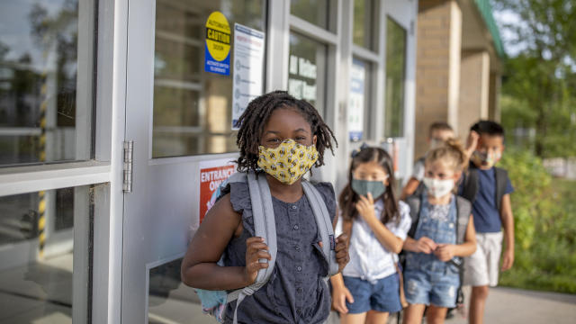 School children with face masks running outside building 