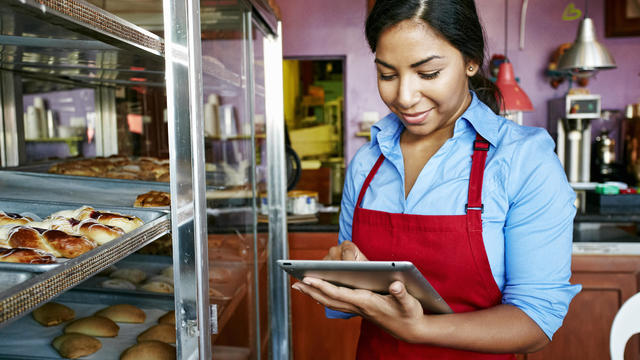 Hispanic waitress taking inventory with digital tablet in bakery 