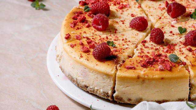 Homemade raspberry baked cheesecake sliced on plate decorated by fresh raspberries and mint over pink marble background with white cloth. Close up 