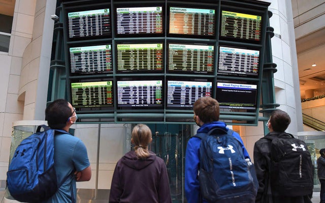 Travelers look at a display board showing cancelled and 