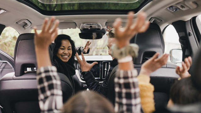 Cheerful family raising hands while enjoying road trip in electric car 