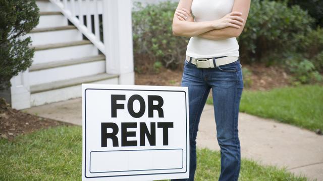 A young woman standing behind a ?for rent? sign 