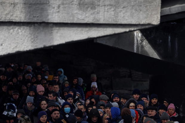 People wait below a destroyed bridge to cross a river as they flee from advancing Russian troops whose attack on Ukraine continues in the town of Irpin outside Kyiv 