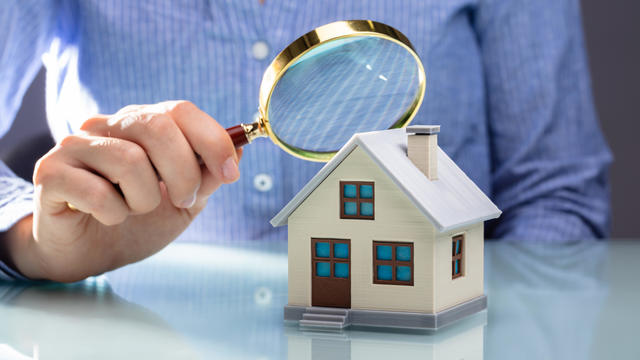 Businesswoman Holding Magnifying Glass Over House Model 