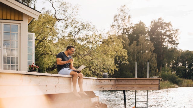 Mature man having juice while using laptop on patio by lake 